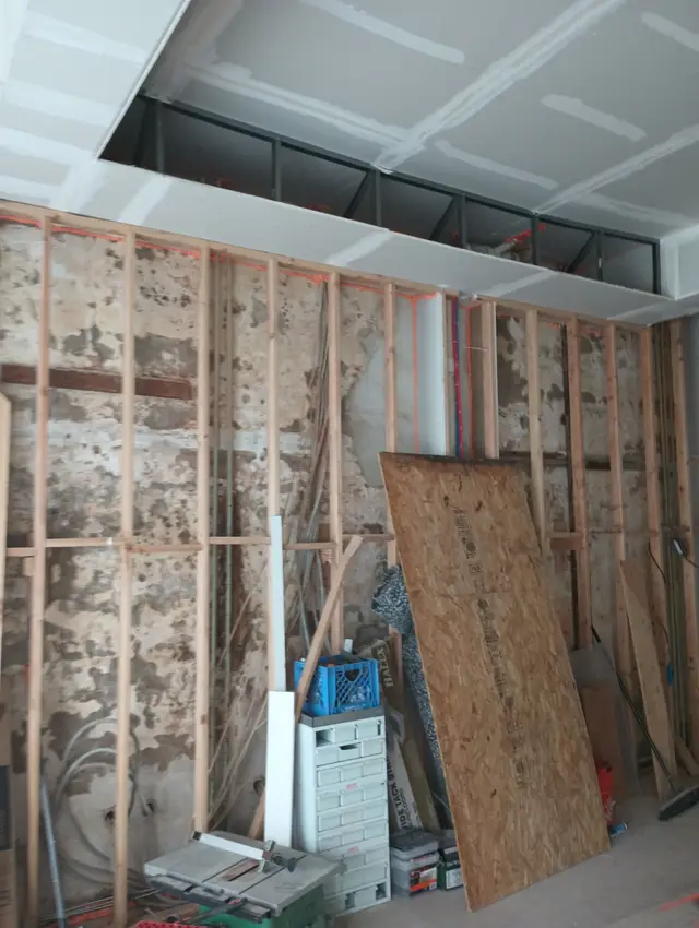 A wall opened down to its studs, with new drywall already hung on the ceiling above.