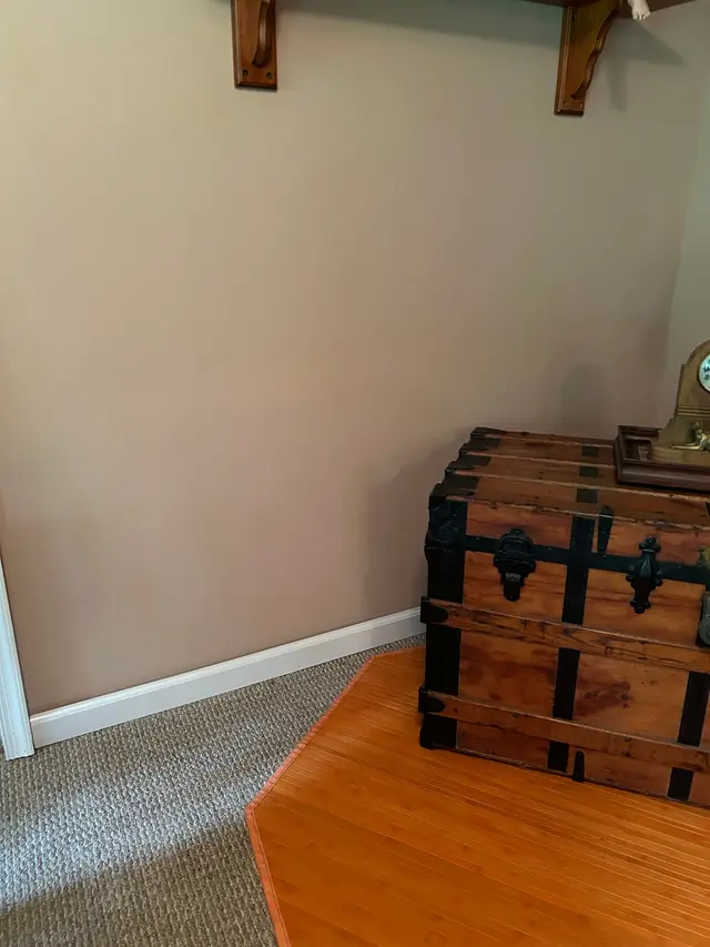 The same wall repaired and painted a soft beige, a wooden trunk sitting against it.