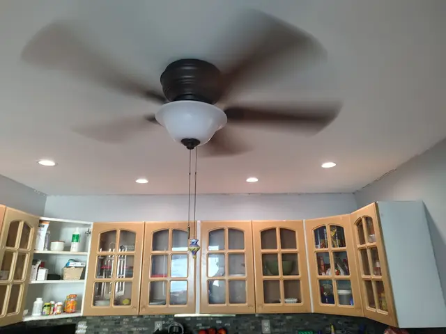 A smooth white kitchen ceiling with recessed lights and a ceiling fan above glass-front wood cabinets.