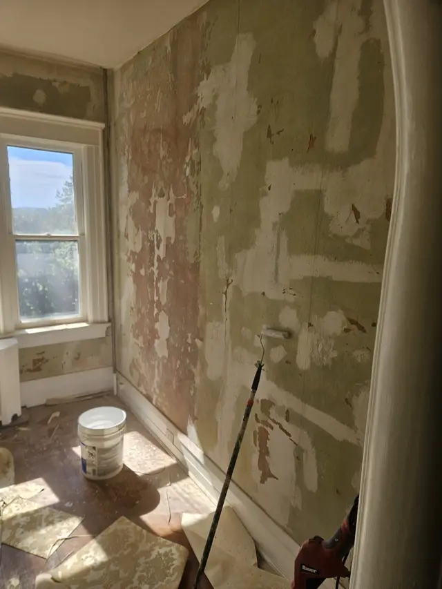 A room in an older house with patched, stained plaster walls and a radiator cover under the window.