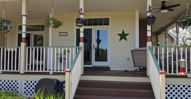 A wide Victorian porch with white rails, painted posts and dark wooden steps leading up to the front door.