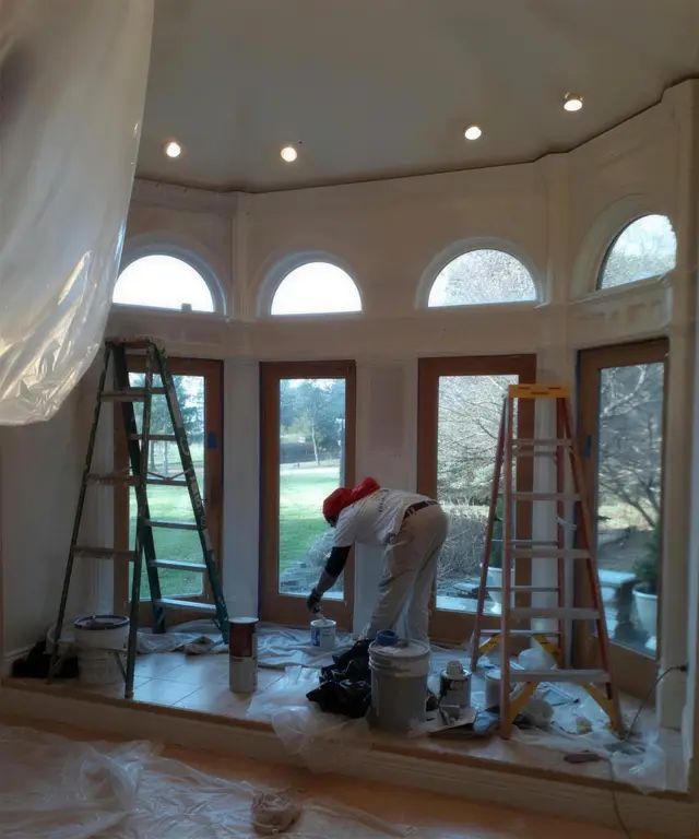 A painter preparing a rotunda of arched French doors, with ladders up and drop cloths laid over the floor.