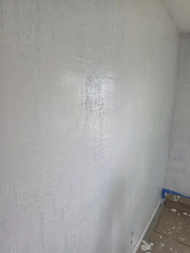 Close-up of a wall part-way through a skim coat, the compound’s knife strokes catching the light.
