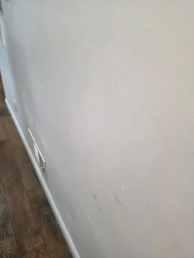 A smooth, freshly finished white wall meeting a wood floor, light raking along its length.