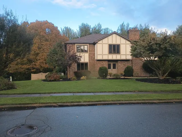 A brick house with Tudor-style half-timbered gables, set back behind a lawn and autumn trees.