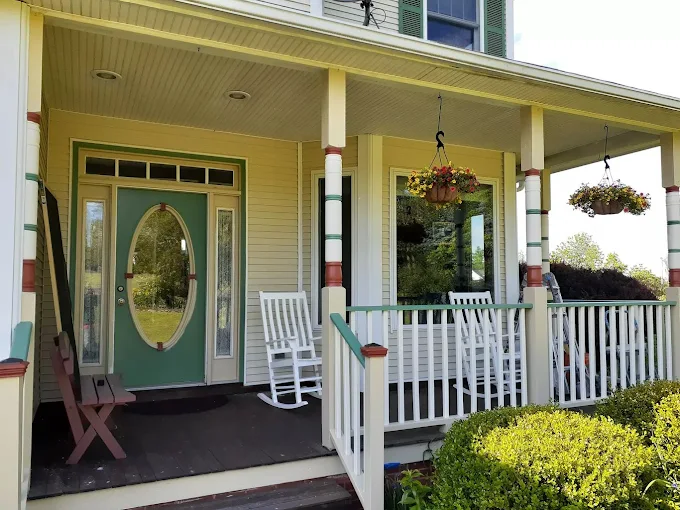 Wraparound porch repaint — cheerful yellow siding, white columns and a welcoming green entry door. Exterior painting & trim.