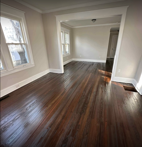 Living and dining room repaint — warm greige walls with crisp white trim and crown moulding over refinished hardwood.