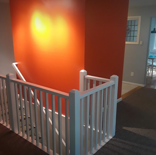 Upstairs landing with a vibrant orange accent wall and a clean white stair railing — interior painting with a smooth finish.