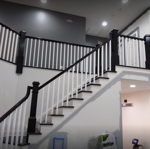 Two-story staircase repaint — crisp white walls with bold black-finished railings, balusters and newel posts. Interior painting & trim.
