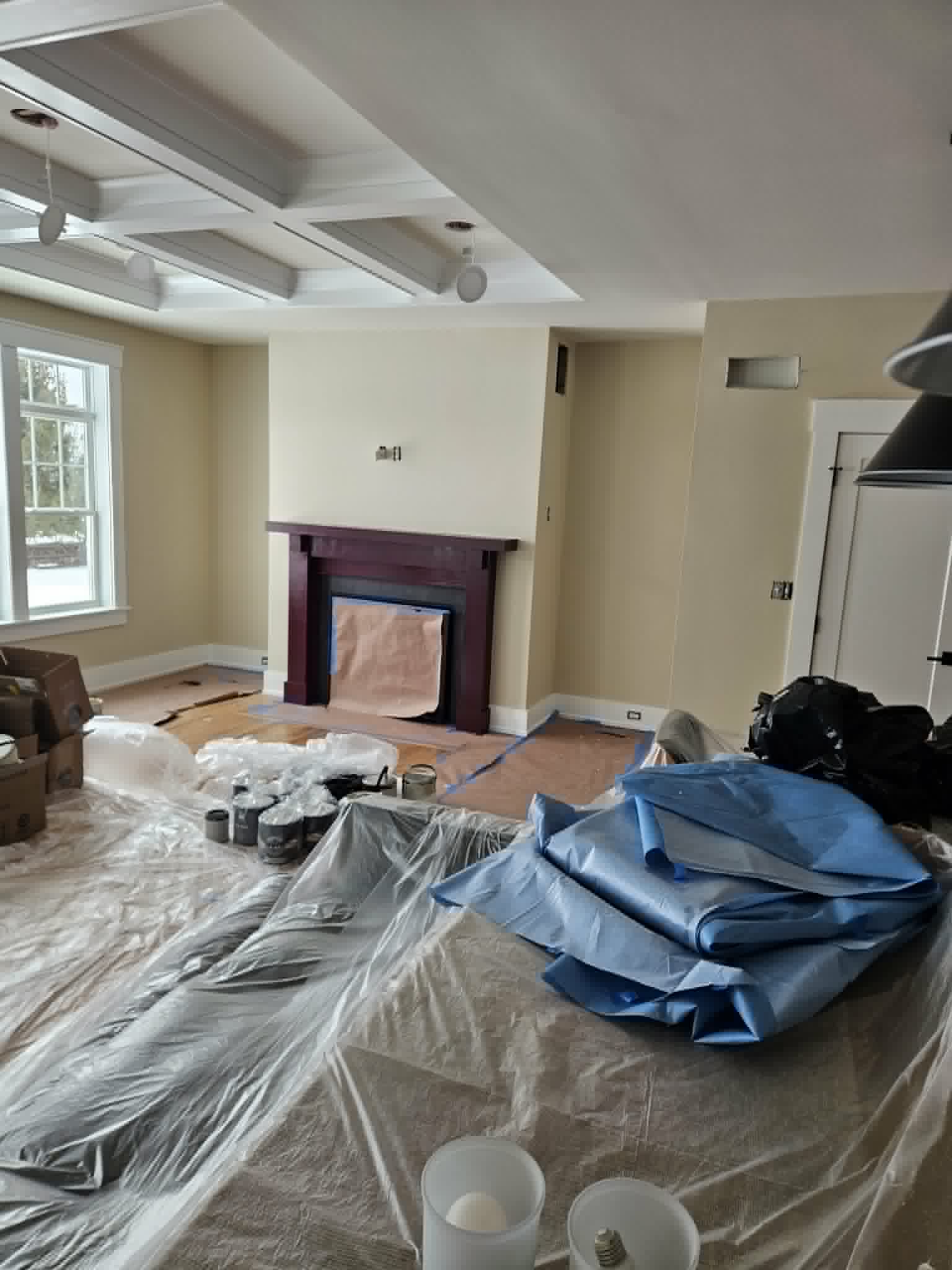 Living room with a rich aubergine fireplace mantel beneath a soft coffered ceiling, draped and in progress — interior painting and trim.