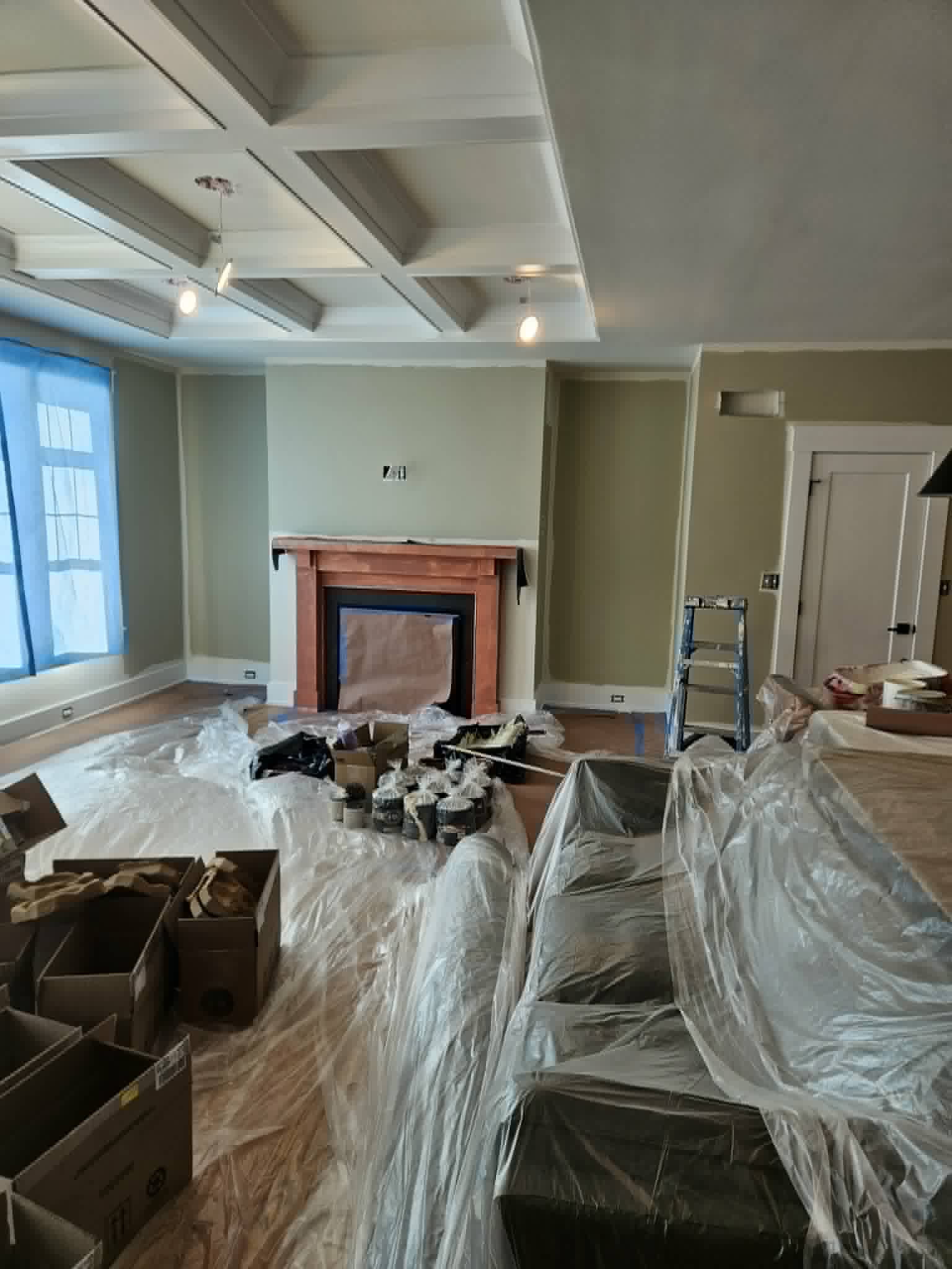 Spacious great room with a freshly painted sage coffered ceiling and matching walls, fully draped and in progress — interior painting.