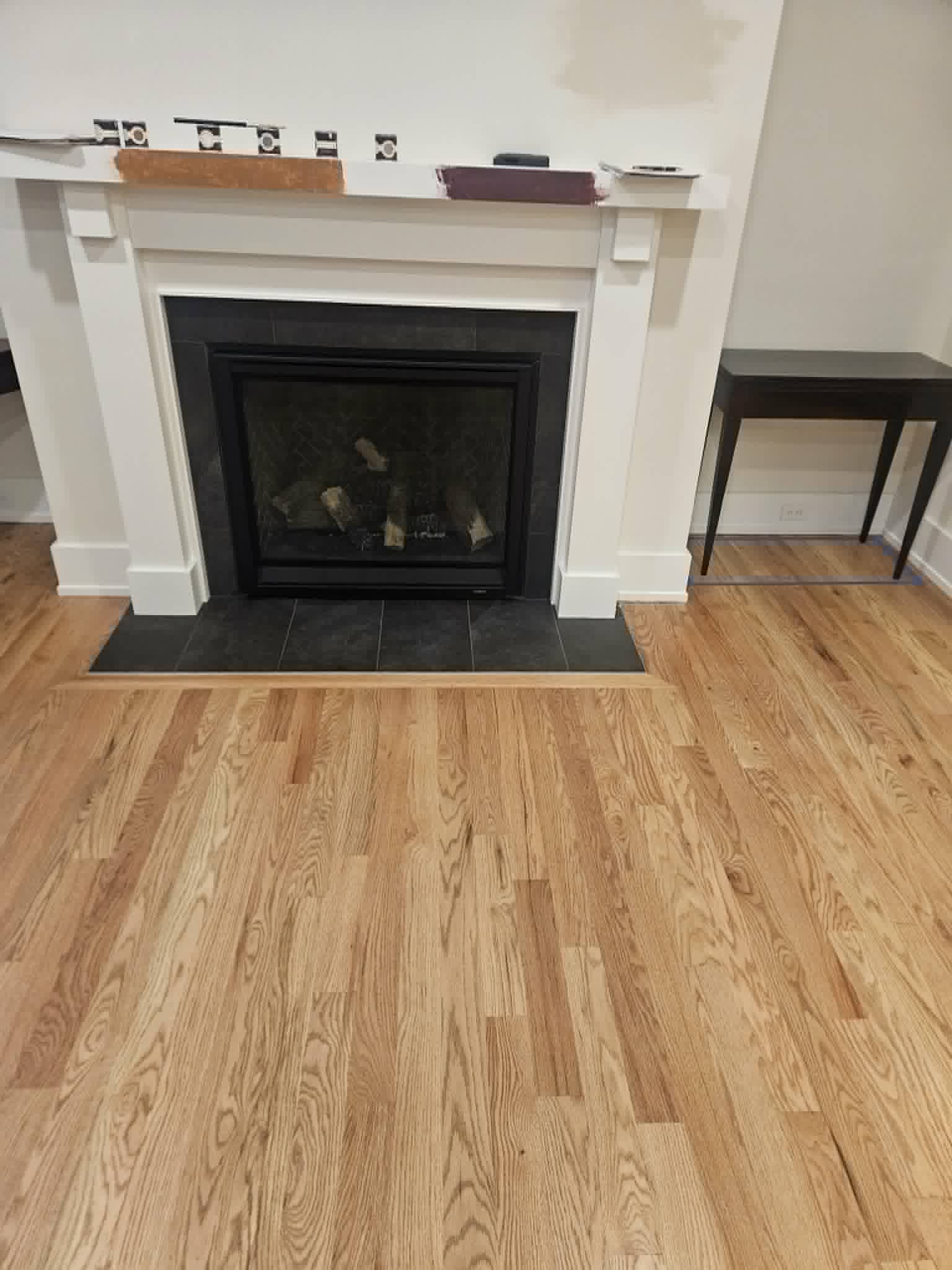 Custom white fireplace mantel with a flawless painted finish over a black-tiled surround and refinished red-oak floor — interior trim and painting.