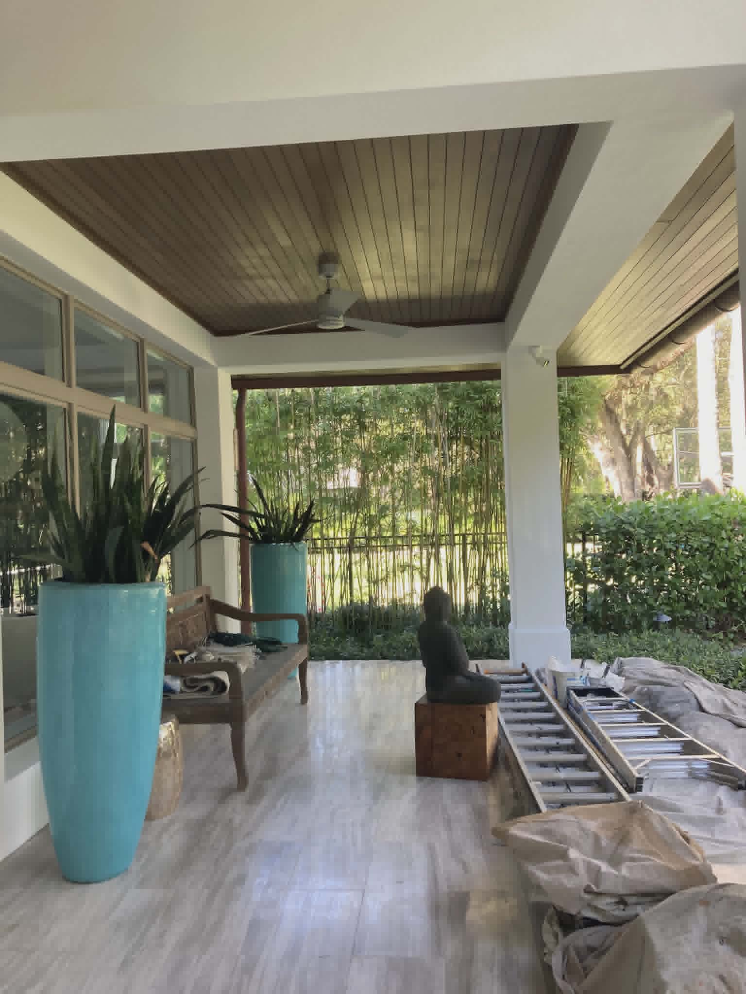 Covered outdoor lanai with a warm stained tongue-and-groove ceiling and bright white beams and columns — exterior painting and woodwork.