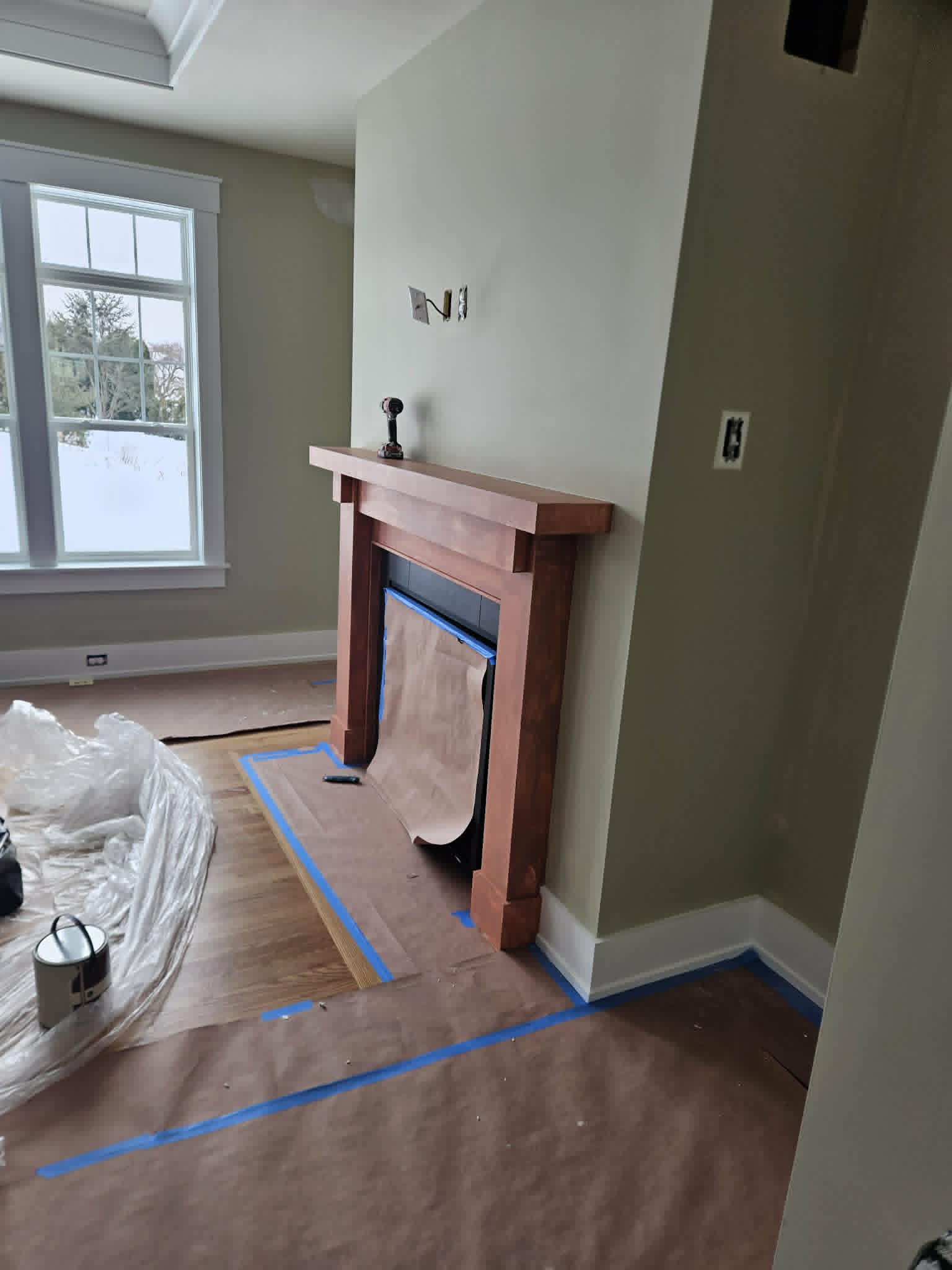 Sage-green room with a stained wood fireplace mantel, floors and surround carefully masked for a clean finish — interior painting and trim.