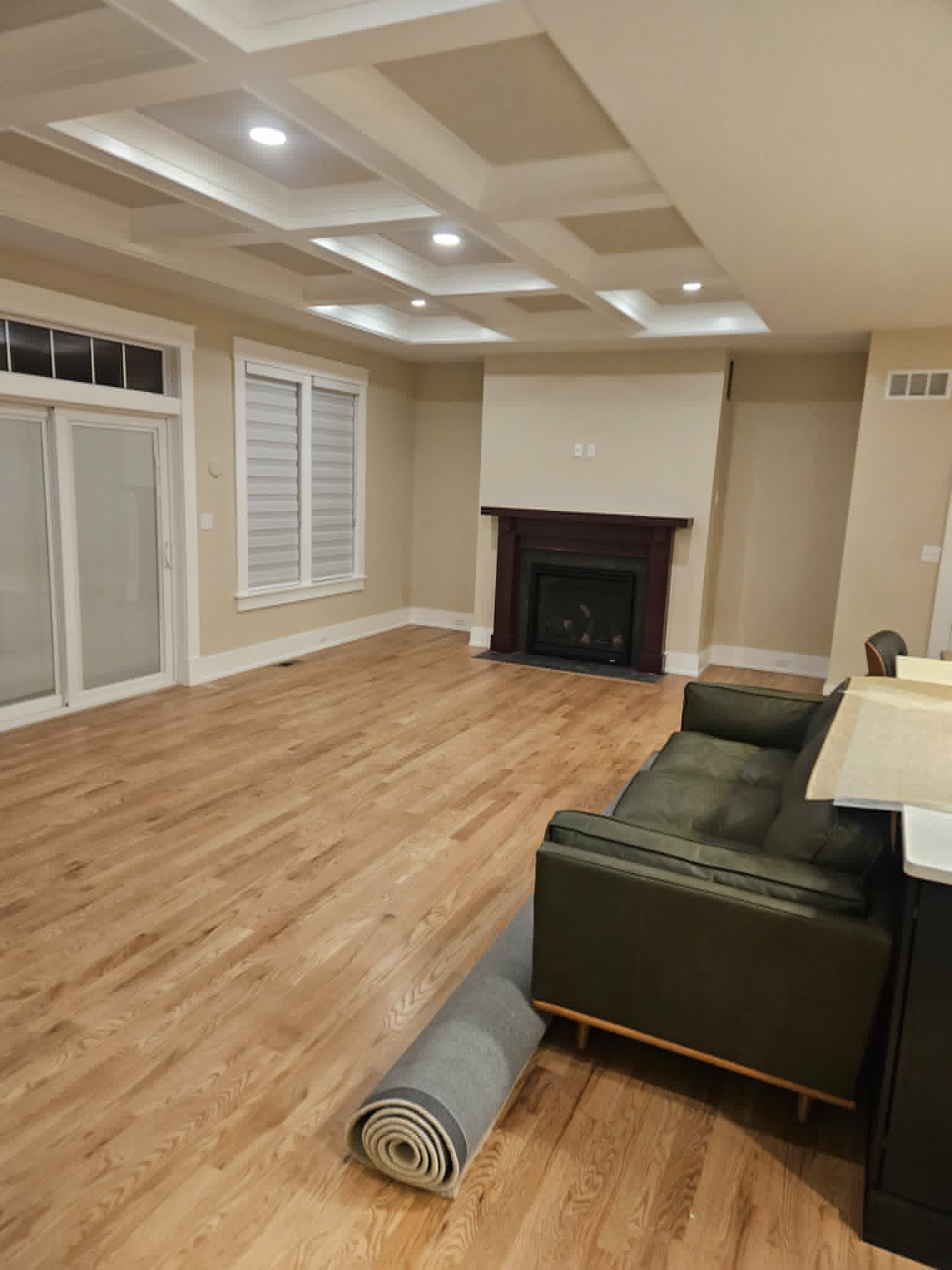 Open-concept living room with a white coffered ceiling, warm neutral walls and a refinished fireplace surround over new wood flooring — interior painting and trim.